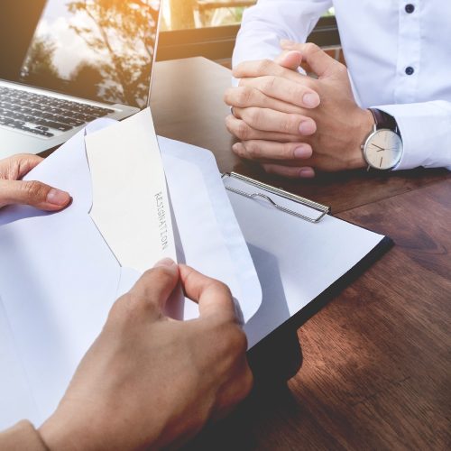 Hand of a businessman hands over a resignation letter on a wooden table to his boss.